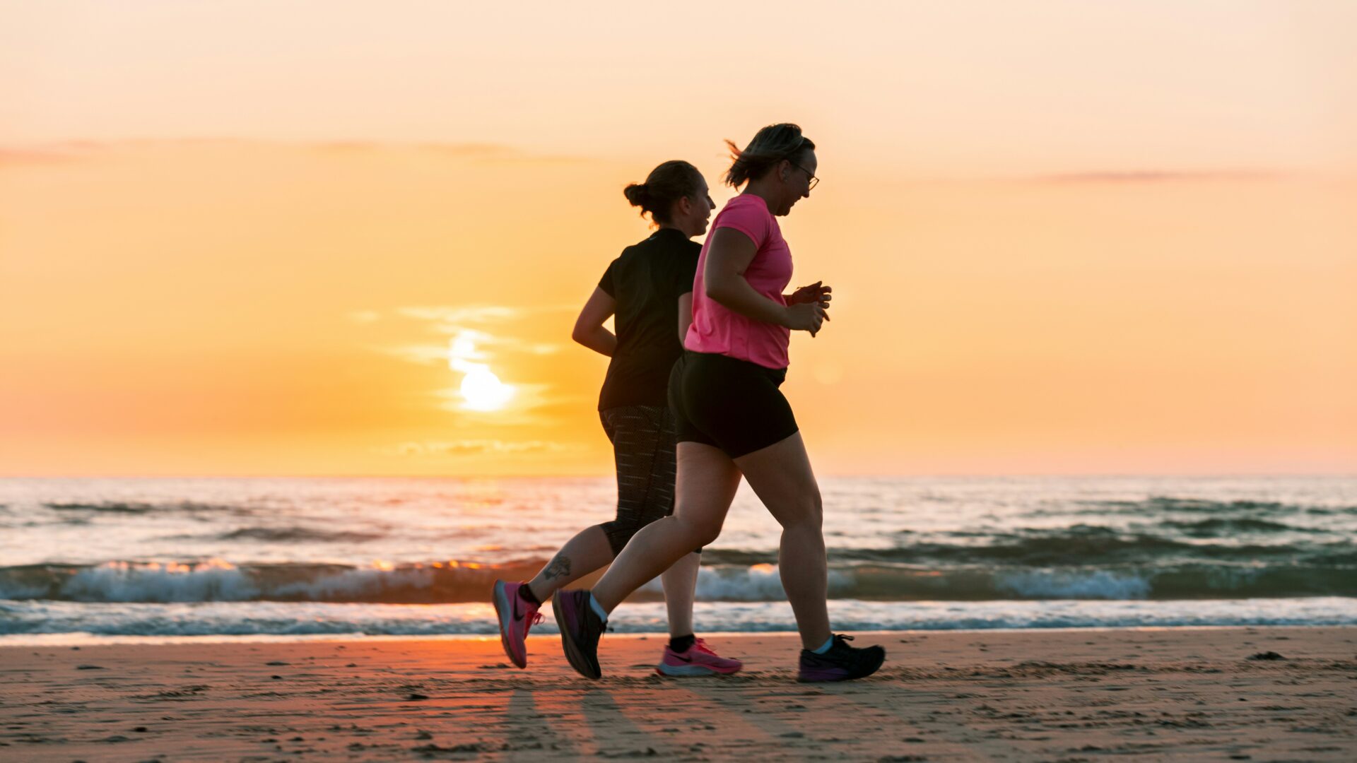 rinke-dohmen-CjOUvHwmdBM-unsplash Two women are running on the beach at sunset.